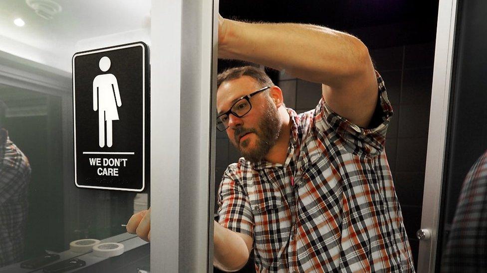 Picture of a man putting up the gender neutral bathroom signs