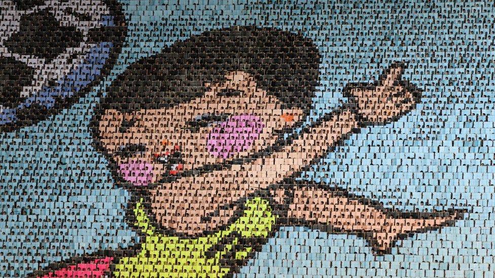 Performers holding up coloured boards creating a big image of a child with football