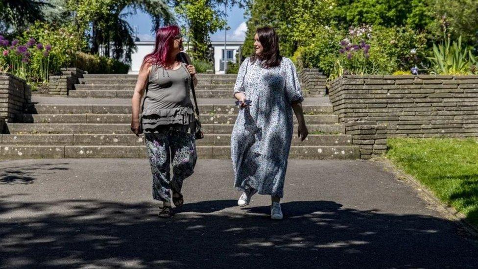 Two people win summery dresses walking in dappled light in the park