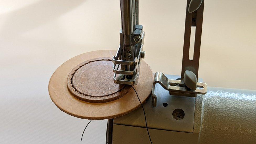 An industrial sewing machine stitching the leather of the muffles together