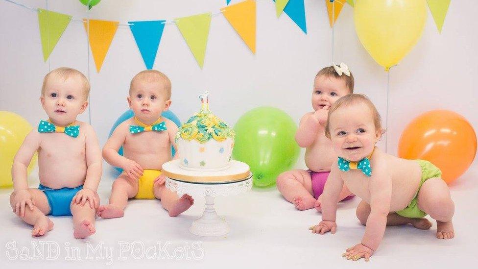 Four babies sit around a birthday cake before they tuck into it