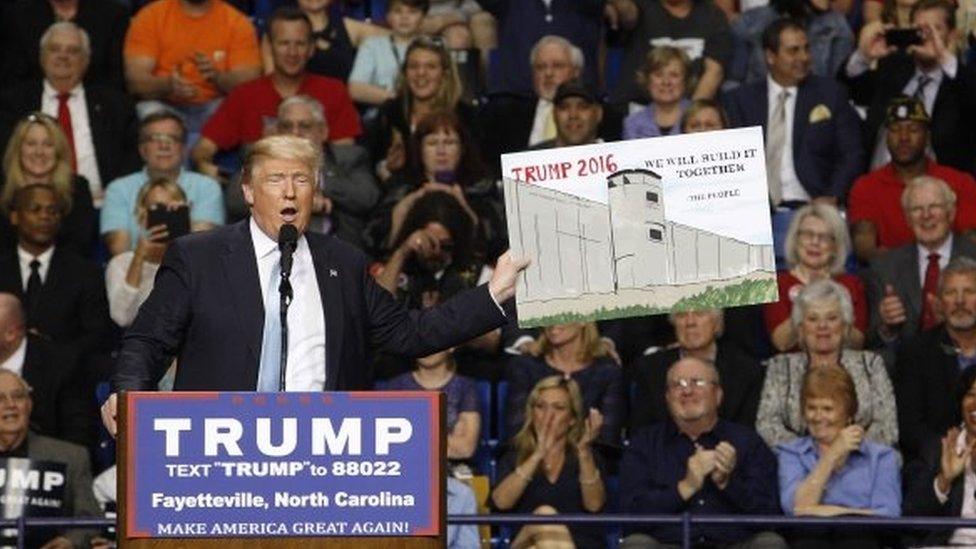 US Republican presidential candidate Donald Trump holds a sign supporting his plan to build a wall between the United States and Mexico that he borrowed from a member of the audience at his campaign rally in Fayetteville, North Carolina March 9, 2016