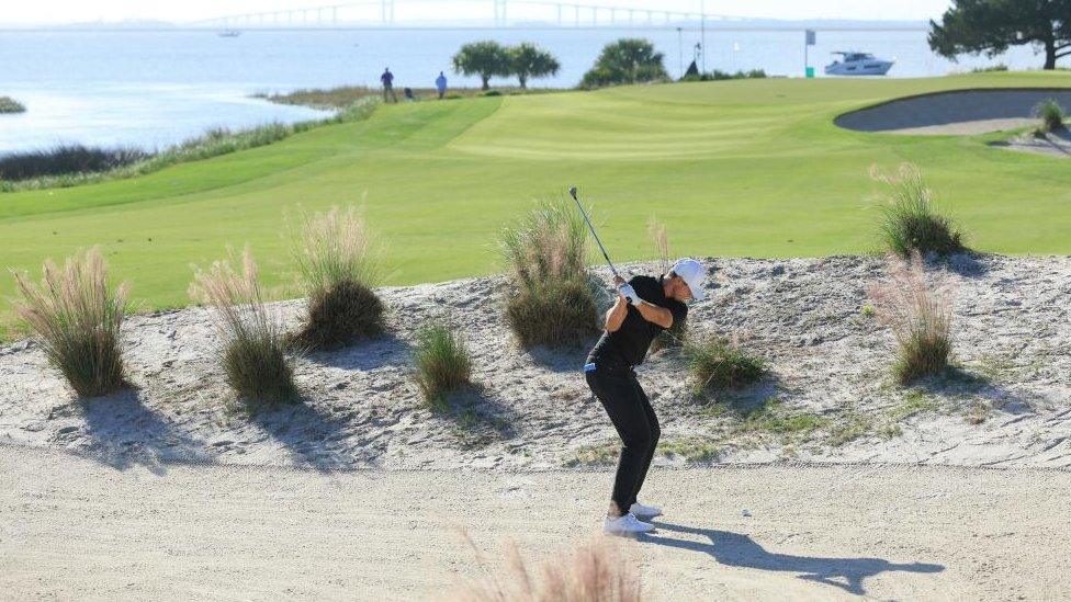 Man takes a swing with a golf club in a bunker on an island