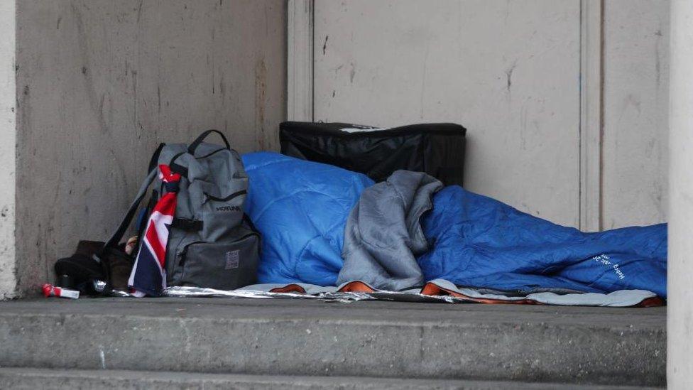 Person sleeping in a shop doorway, covered in a sleeping back