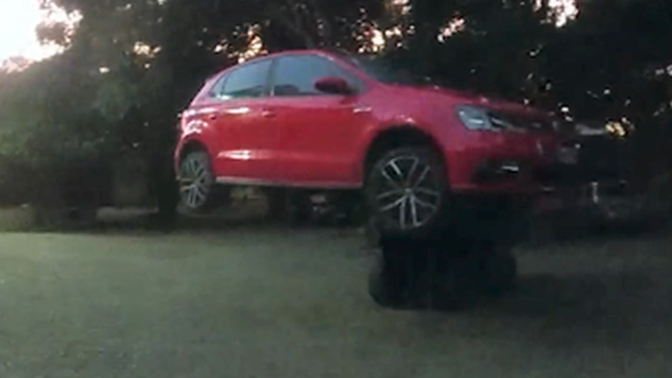 A red car suspended in the air by a forklift