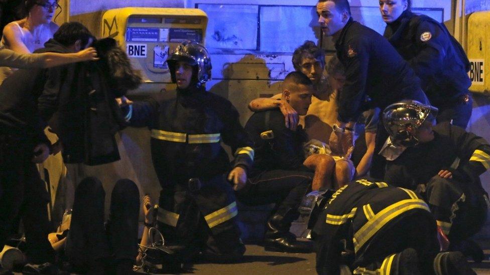 French fire brigade members aid an injured individual near the Bataclan concert hall following fatal shootings in Paris