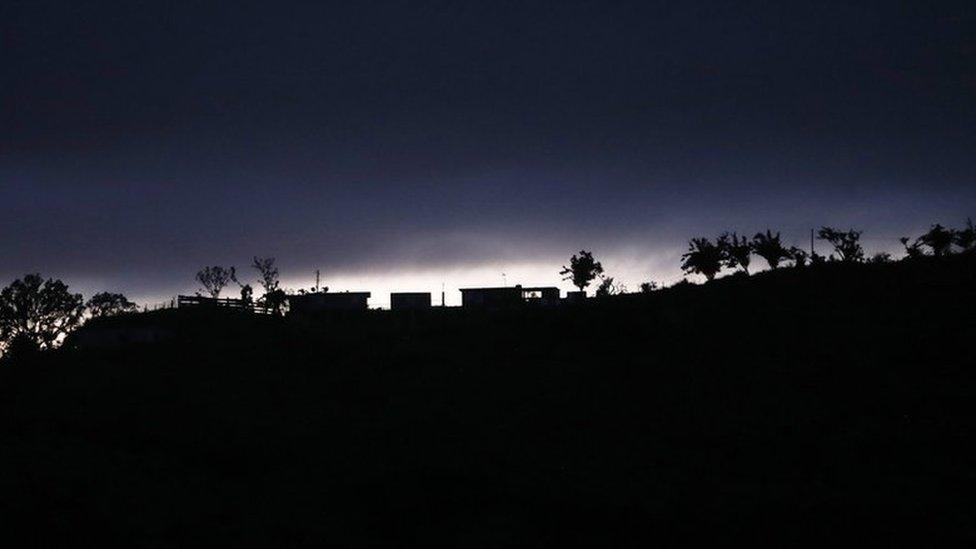 Structures and trees line a section of a populated ridge normally lit with electricity, as dusk falls in Morovis, Puerto Rico.