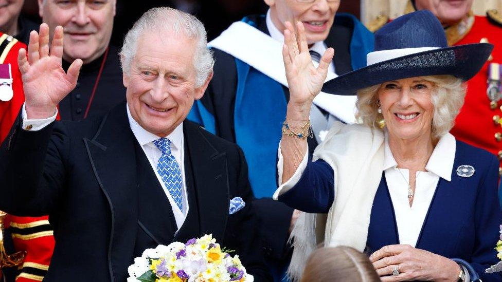 King Charles and Queen Camilla, waving, with staff behind