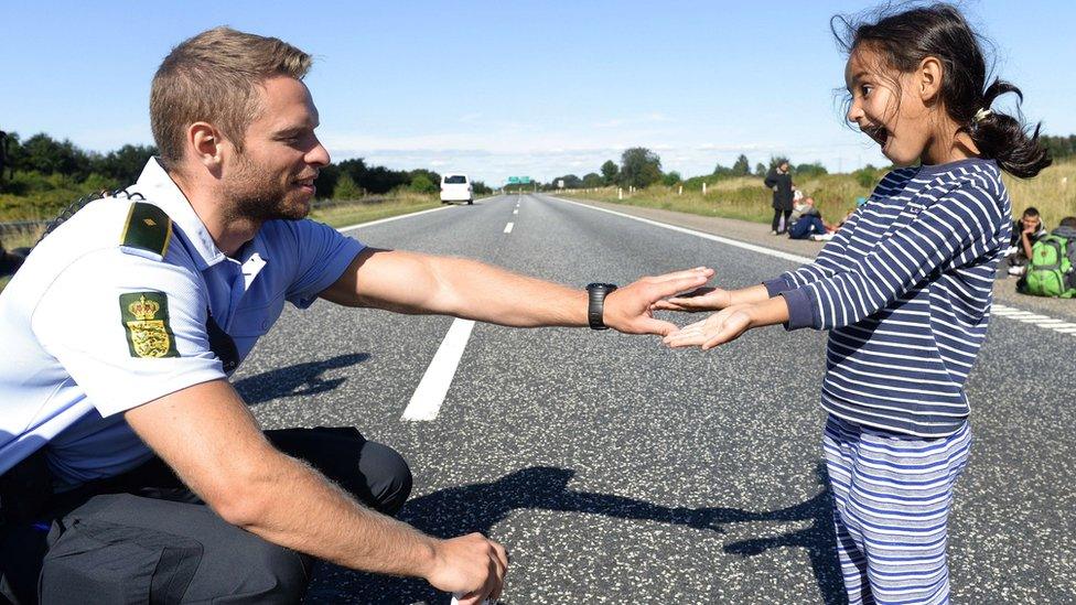 Danish policeman plays with child as migrants walk from Padborg, on Danish-German border, towards Sweden. 9 Sept 2015