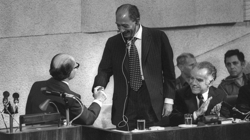 This handout file photo provided by the Israeli Government Press Office (GPO) shows Egyptian President Anwar Sadat standing to shake hands with Israeli Prime Minister Menachem Begin (L) in the Knesset, the Israeli parliament, as Speaker Yitzhak Shamir applauds, after he arrived in Jerusalem in a surprise visit on 20 November 1977