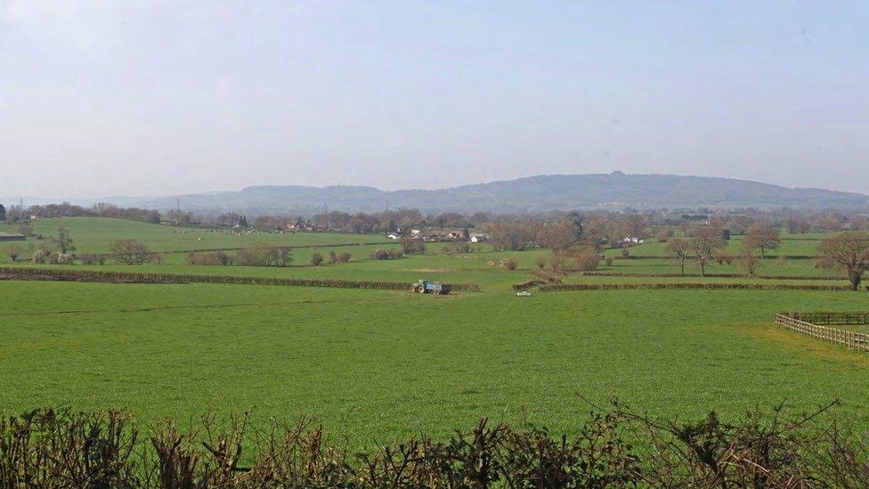 Image showing the land near Highleadon where JBM Solar Projects 21 Ltd wants to create a solar farm. There are very few houses on the large field and a blue tractor in the middle of it. More fields can be seen in the distance.