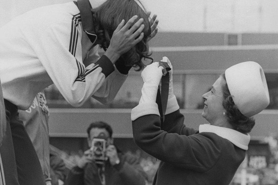 Queen Elizabeth gets the ribbon entangled in the hair of Debbie Brill of Canada, as she presents her with the gold medal for the high jump at Meadowbank Stadium, during the Commonwealth Games in 1970