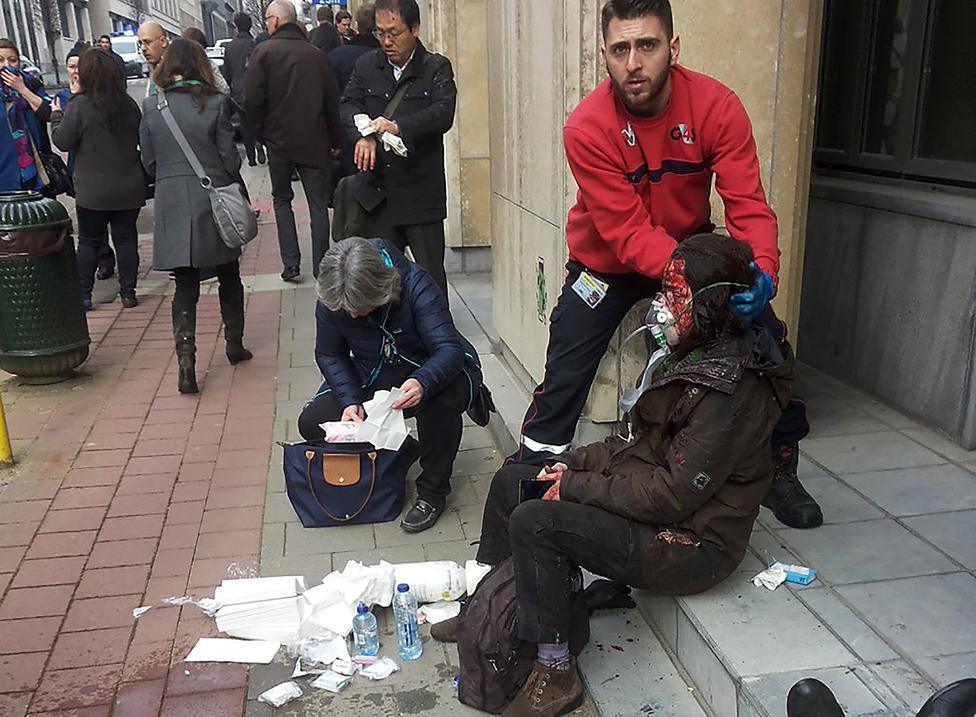 A private security guard helps a wounded women outside the Maalbeek - Maelbeek metro station in Brussels on March 22, 2016 after a blast at this station located near the EU institutions.