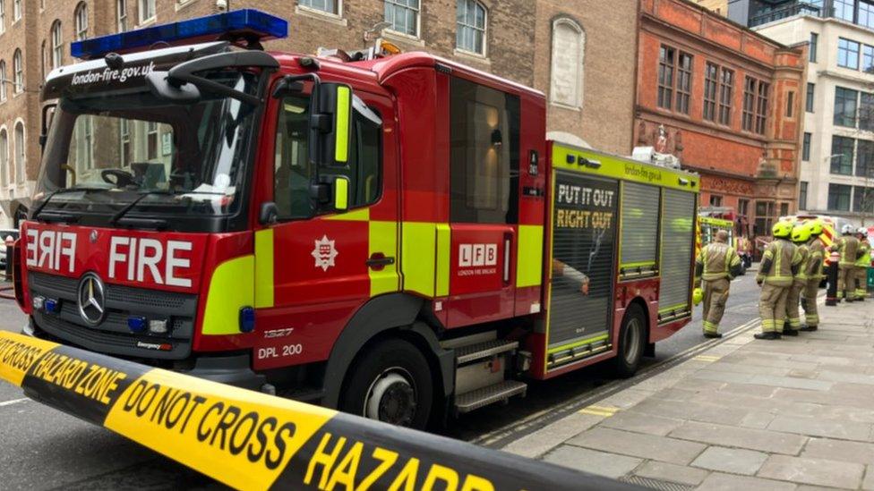 Fire engine behind hazard tape, with firefighters in the distance