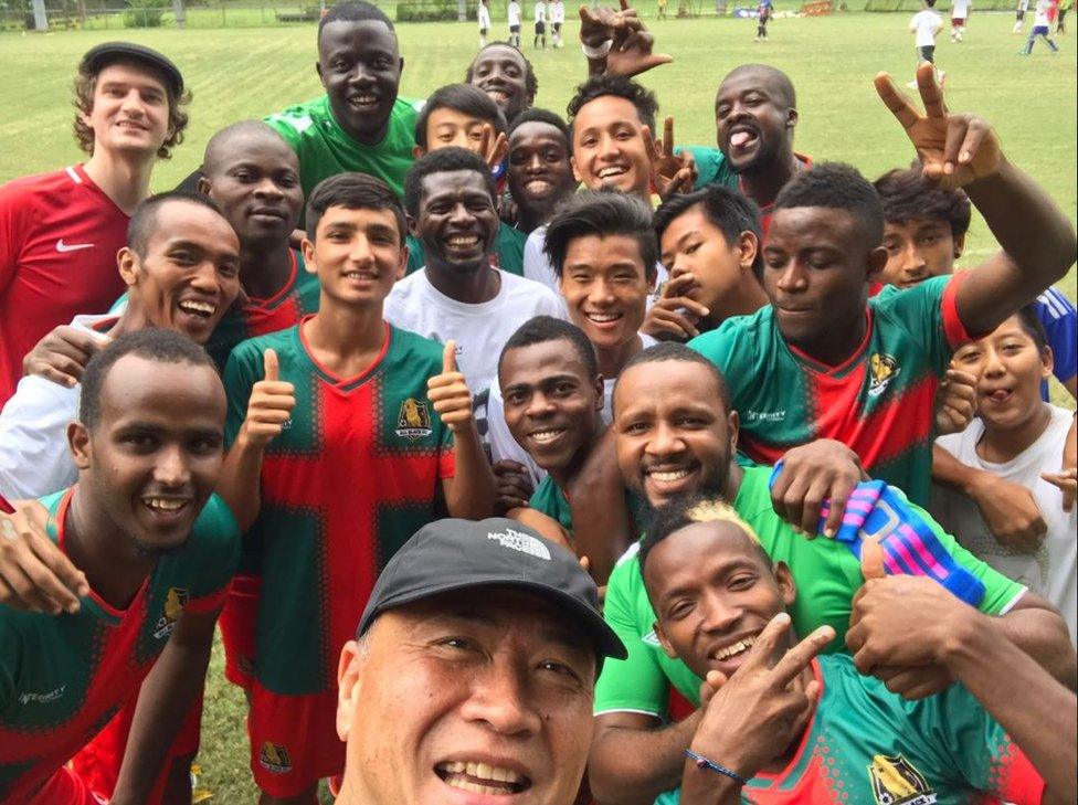 The team smile and make thumbs up and peace signs in a group selfie