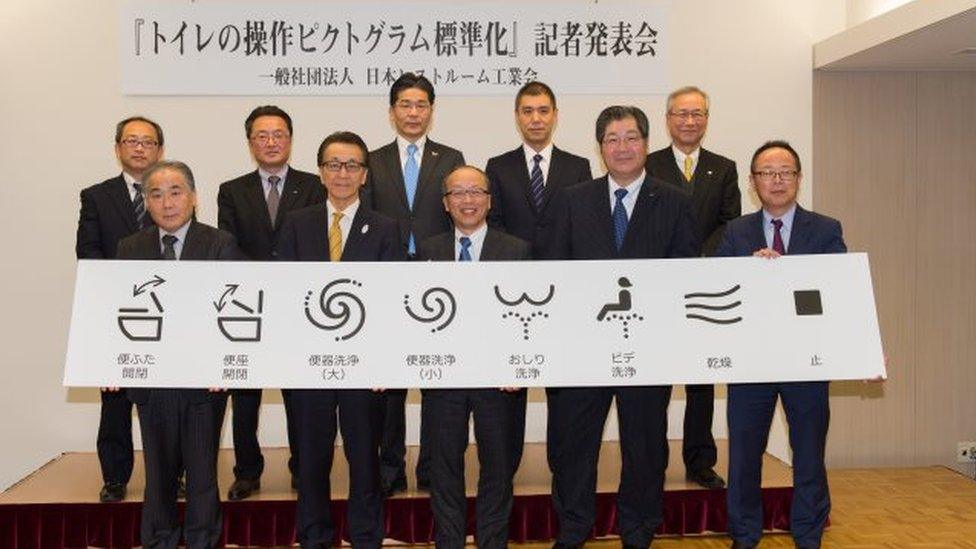 Senior members of the association hold up the new symbols, which are, from left, raise the lid, raise the seat, large flush, small flush, rear spray, front spray, dry, and stop