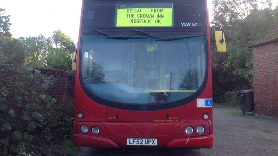 The red bus with a sign saying Hello from The Crown Inn, Norfolk UK