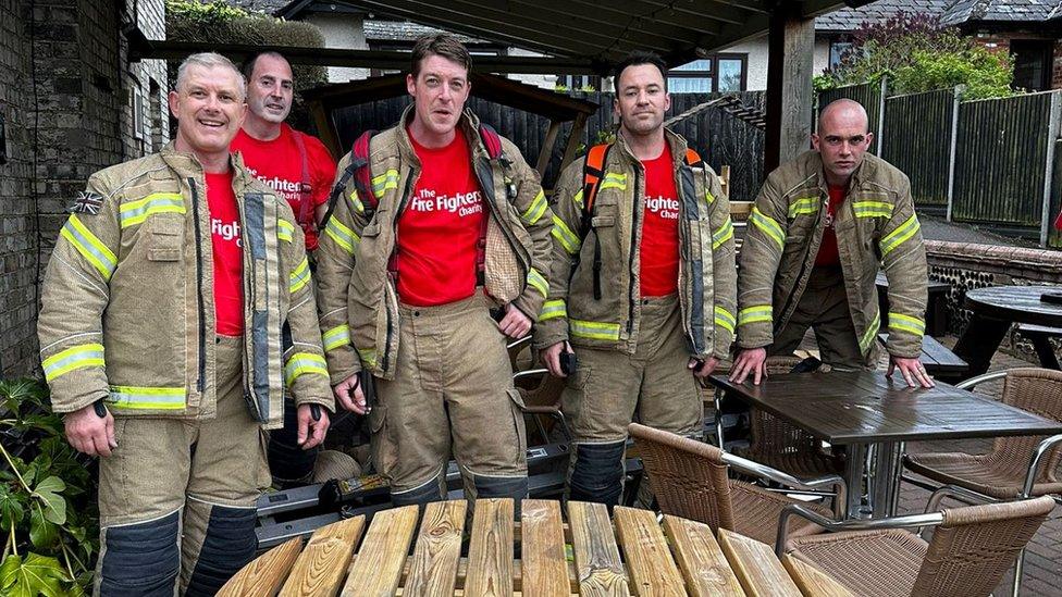 Firefighters wearing their tunics stand around a table