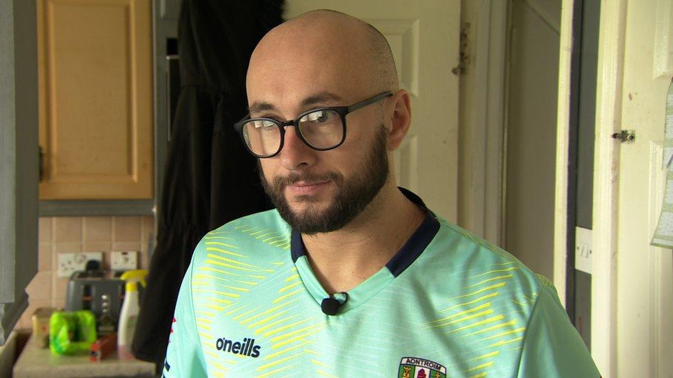 Christopher Stephens, wearing a green GAA jersey and glasses, looks at the camera