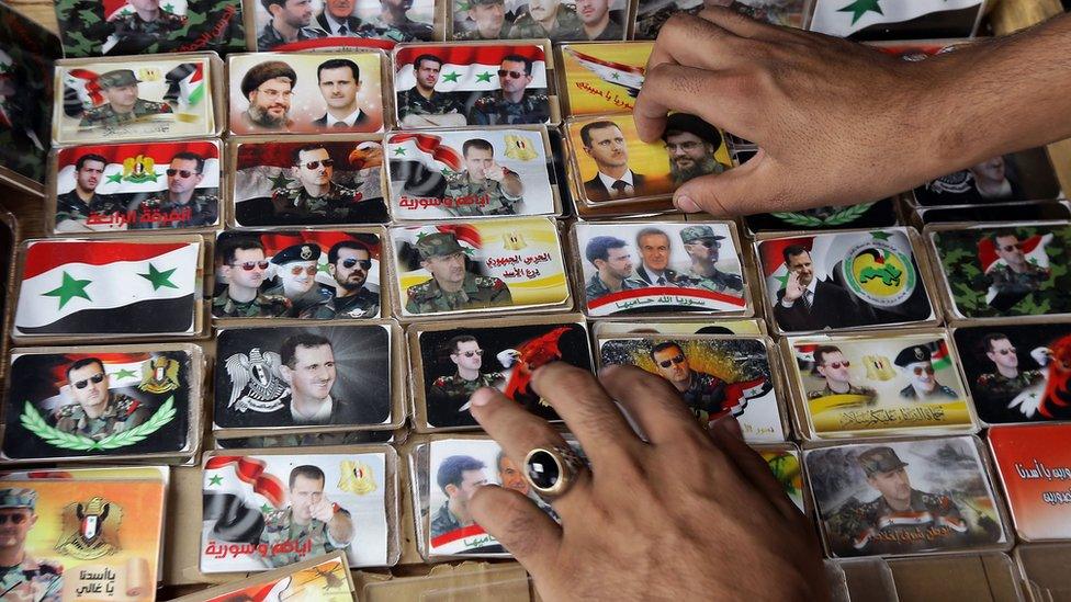 A vendor displays cards of President Bashar al-Assad and his family in Damascus (22 October 2015)
