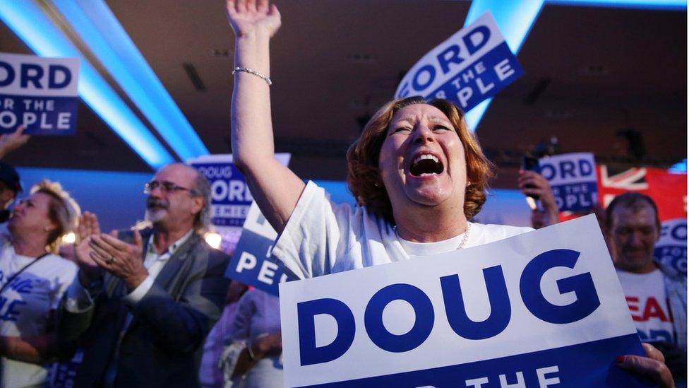 A woman cheers while holding a Doug Ford campaign sign