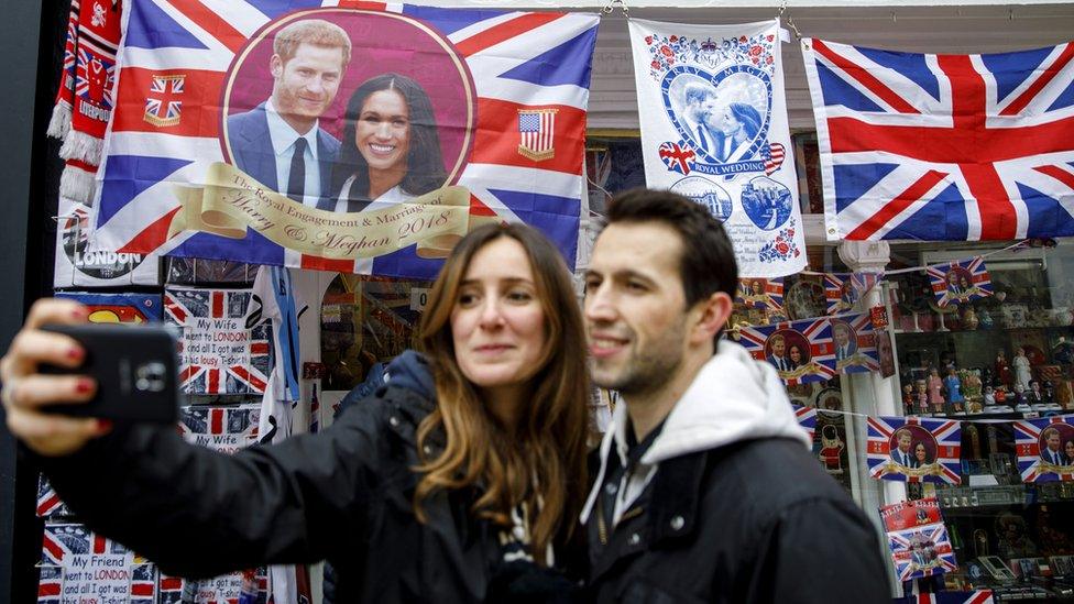 Tourists take a photograph in front of souvenirs featuring Prince Harry and Meghan Markle in a gift shop in Windsor.