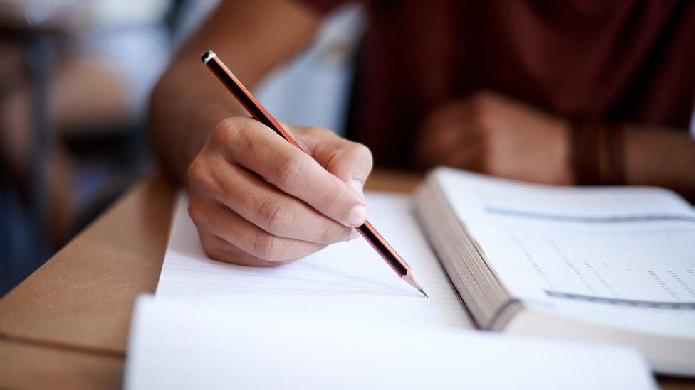 photograph shows a person holding a pencil while sat at a desk for an exam