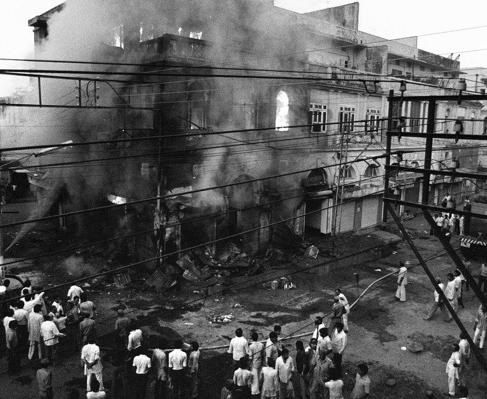 People watch as a building belonging to Sikhs burns in Delhi. Photo: 2 November 1984