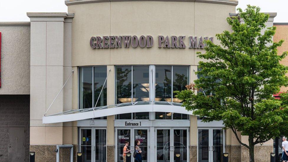 A group of people wait outside of an entrance to Greenwood Park Mall on 18 July 2022