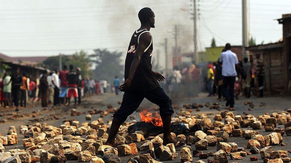 A man walks through paving stones and a tire fire during protests against the governing party on June 26, 2015 in Bujumbura, Burundi