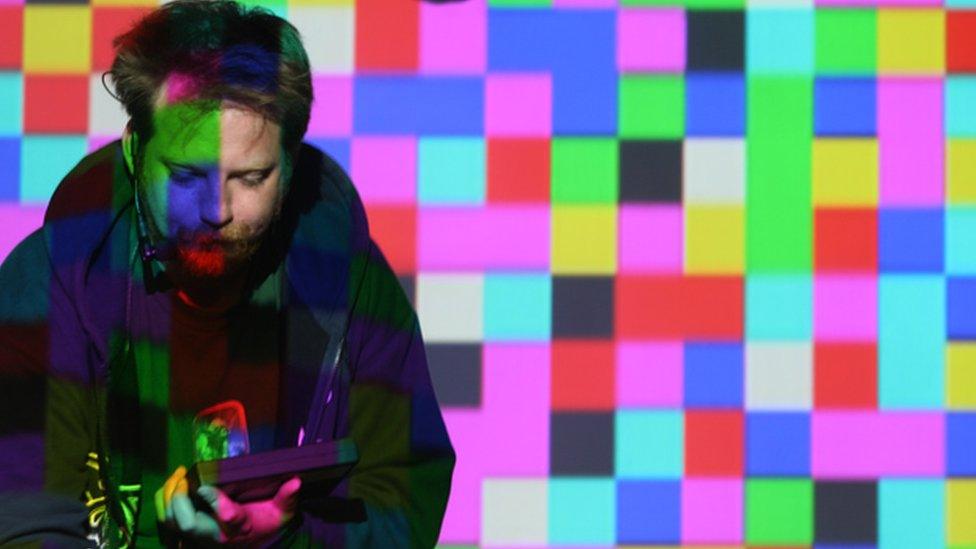 A man in front of colourful square lights looks at a handheld device