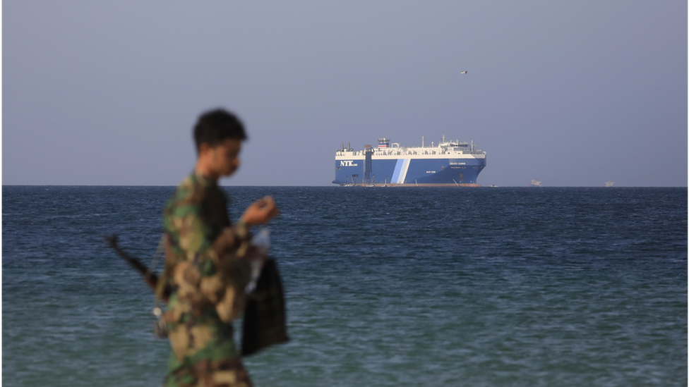 A Houthi soldier walks along the beach with the Galaxy Leader cargo ship in the background, seized by the Houthis offshore of the al-Salif port on the Red Sea in the province of Hodeidah, Yemen, 05 December 2023.