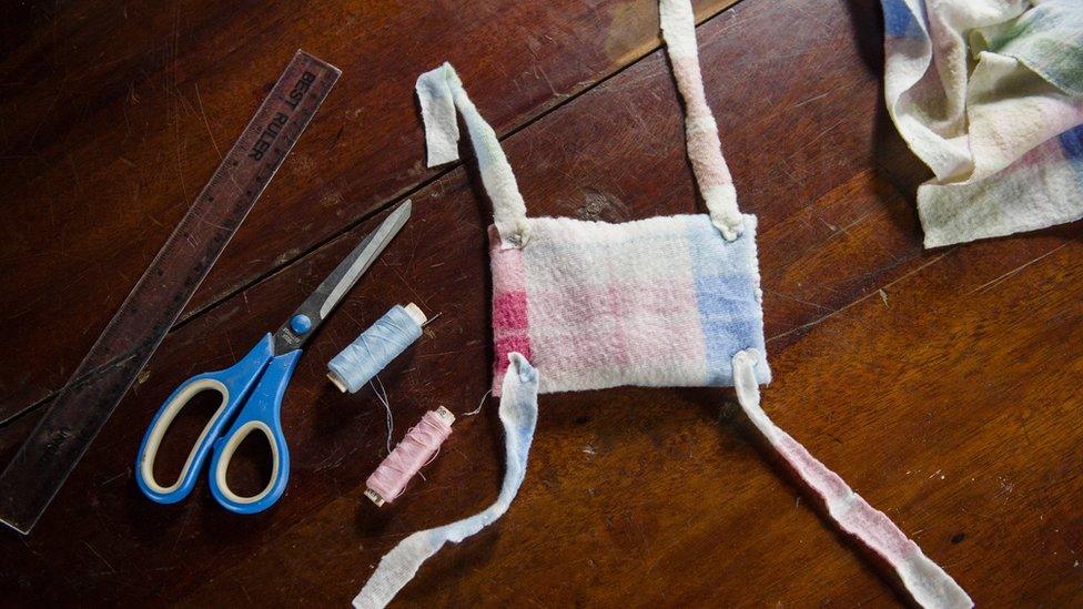 A makeshift absorbent pad with four fabric strips sits on a table, surrounded by the materials used to make it - cloth, a ruler, scissors, and thread