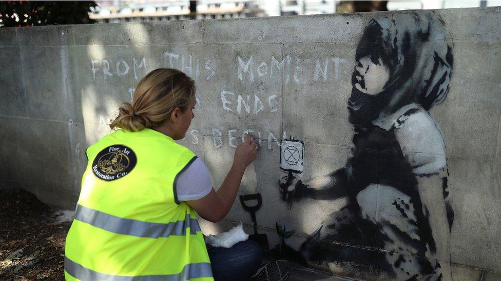 Mural being cleaned by woman wearing Fine Art Restoration Company jacket