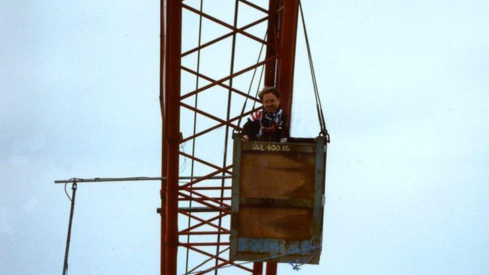 Mr Brien standing with his camera inside a small wooden box suspended high in the air by the crane.