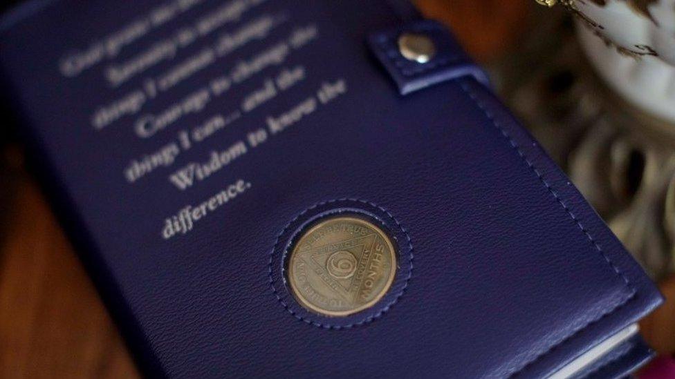 A copy of AA's Big Book with a leather cover and a six month sobriety coin