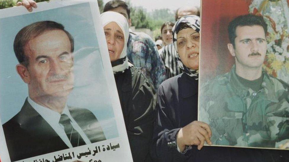 Syrian women carry portraits of Hafez and Bashar al-Assad in Damascus in June 2000