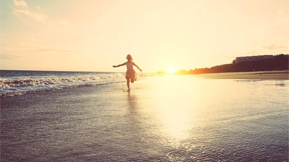 Happy little girl running inside water on the beach at sunset -