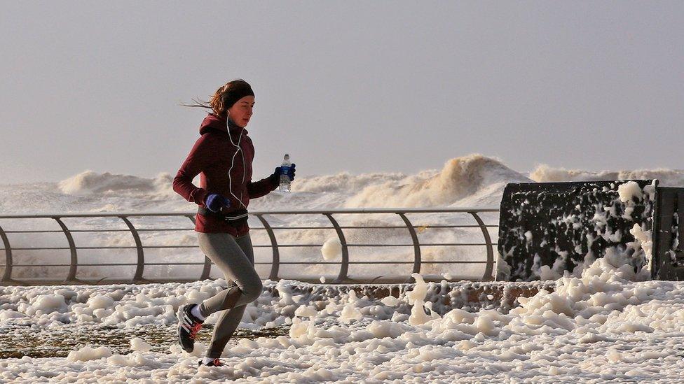 Woman running in sea foam in Blackpool, after Storm Eleanor