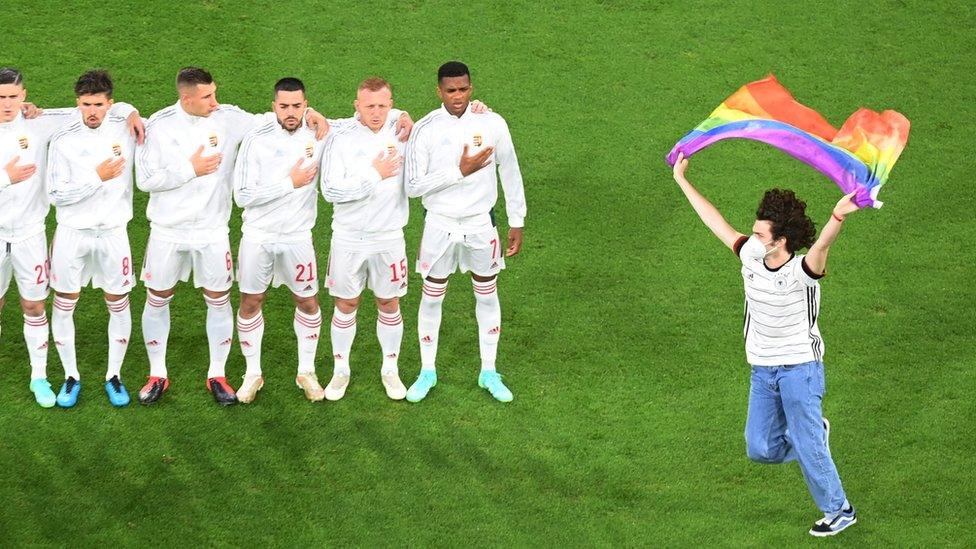 spectator with rainbow flag runs past Hungary players.