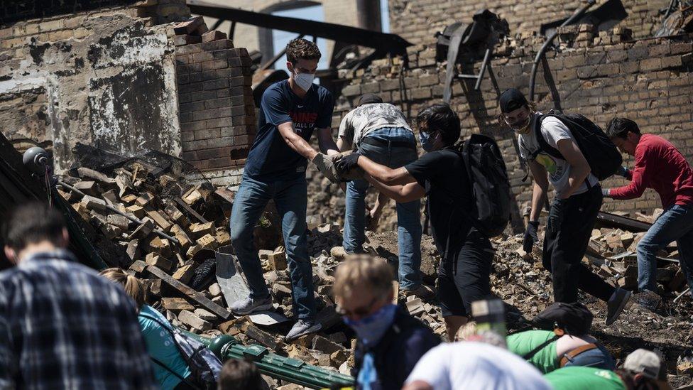 People hand rubble to each other in the ruins of a burned building in Minneapolis