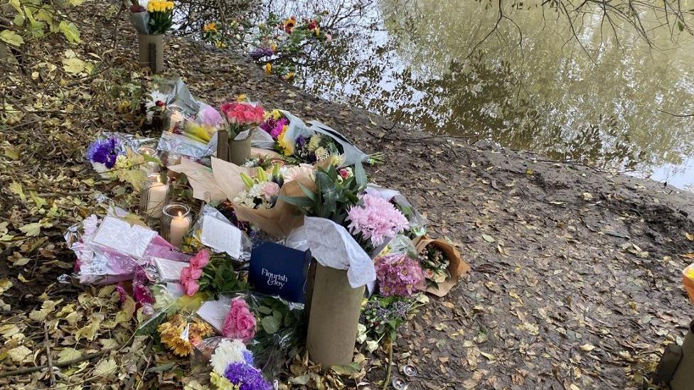 Bunches of flowers, candles and cards are left by the river