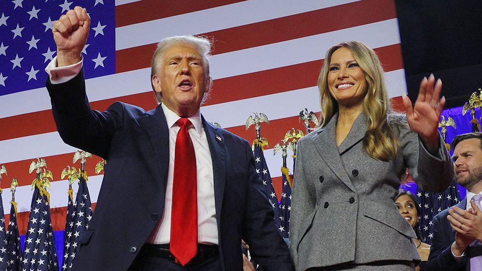 Donald Trump raises a fist onstage during his rally, as he stands next to Melania waving with the backdrop of the US flag behind them