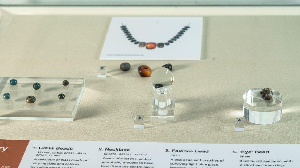 View of Bronze Age beads on display, including blue/green glass beads, a faience bead and a photograph of a replica of a necklace at Peterborough Museum