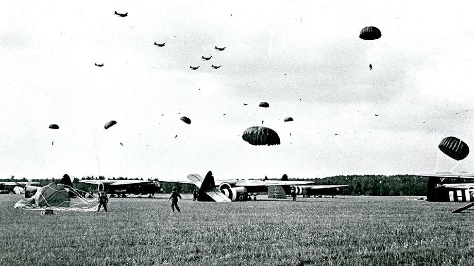 Black and white image of paratroopers being dropped in a field with gliders on the ground in Arnhem in the Netherlands in September 1944