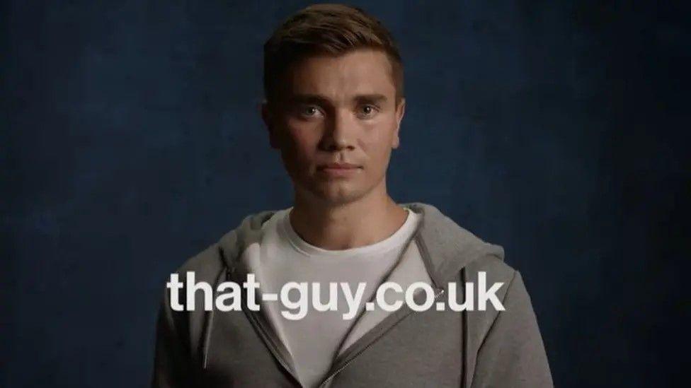 Grab from the advertising campaign video. It shows a young man in a white t-shirt and grey hoodie looking directly at the camera. There is a strapline that says that-guy dot co dot uk