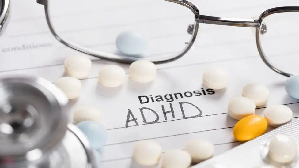 A pair of glasses on a piece of paper saying "Diagnosis ADHD" and some pills. 