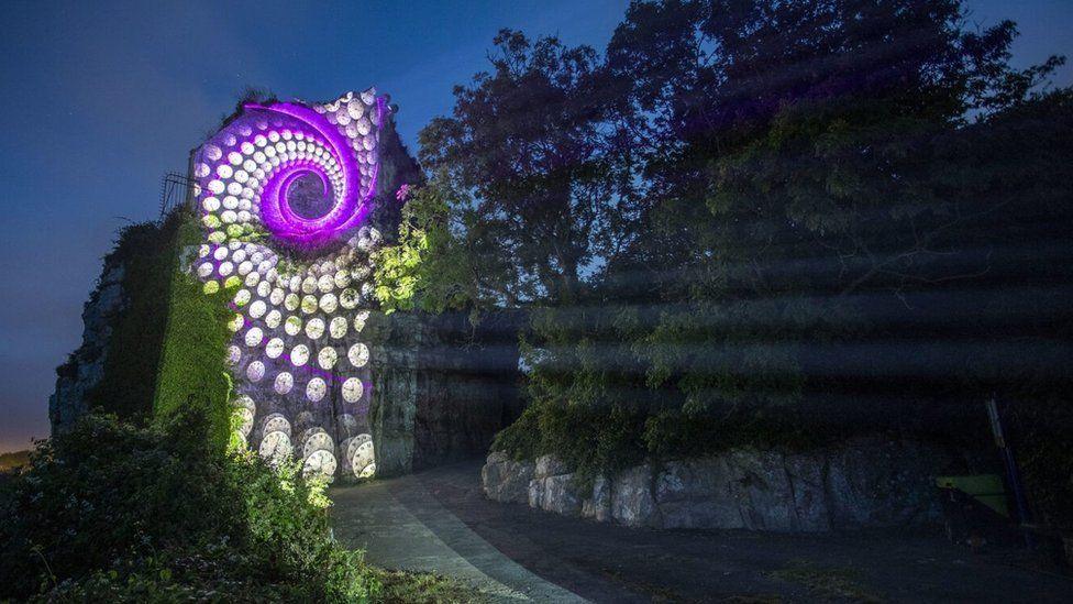 A light effect on a rock in Portland of white and purple lights create a swirling shell-like effect