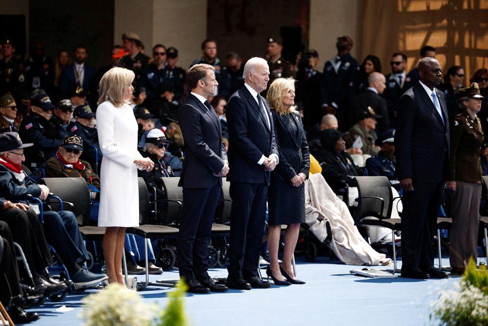 US President Joe Biden (C), US First Lady Jill Biden (R), France's President Emmanuel Macron (2nd L) and French President's wife Brigitte Macron (L) stand to attention during the US ceremony marking the 80th anniversary of the World War II "D-Day" Allied landings