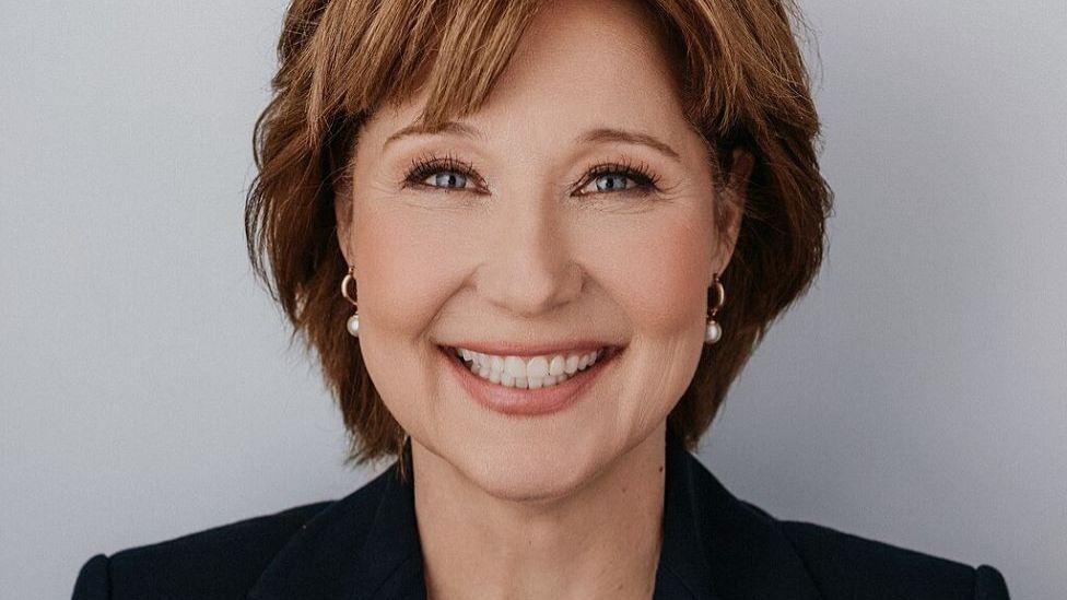 A smiling Christy Clark wearing a smart, black jacket and white earrings.